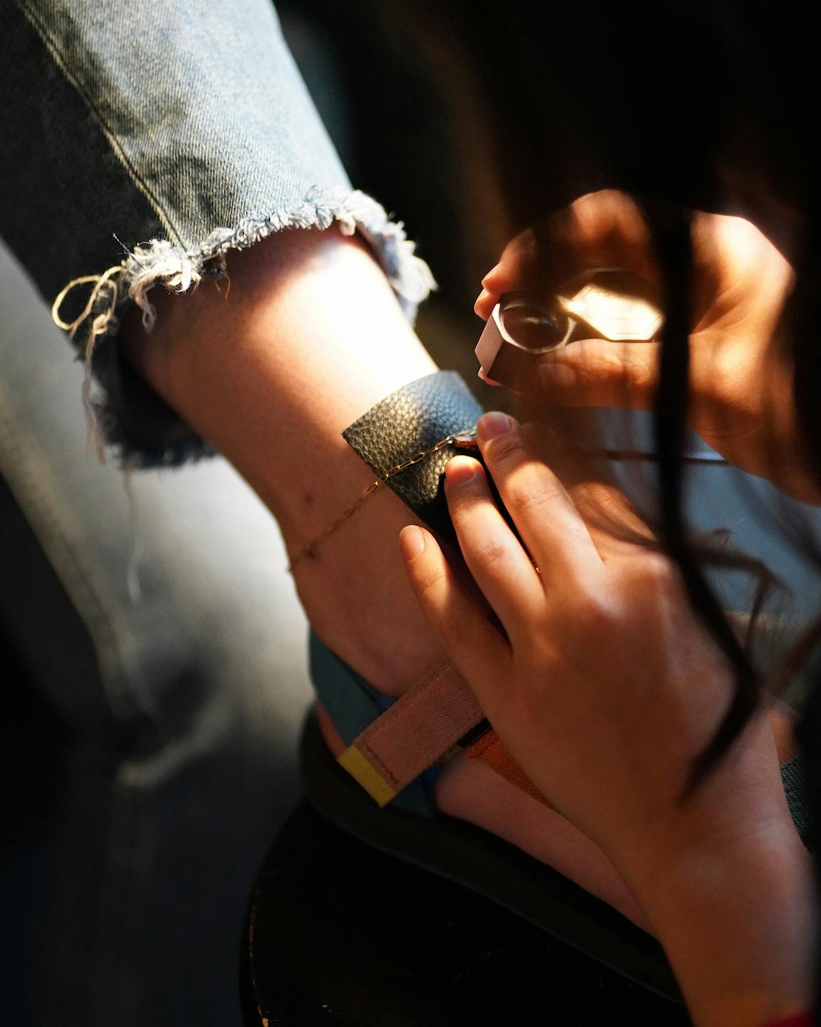 A person looks through a jeweler's loop at a chain on someone's ankle.